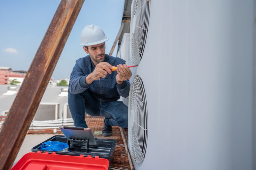 Technician performing HVAC repairs on rooftop unit, using tools and tablet for diagnostics, emphasizing expertise in older home systems.