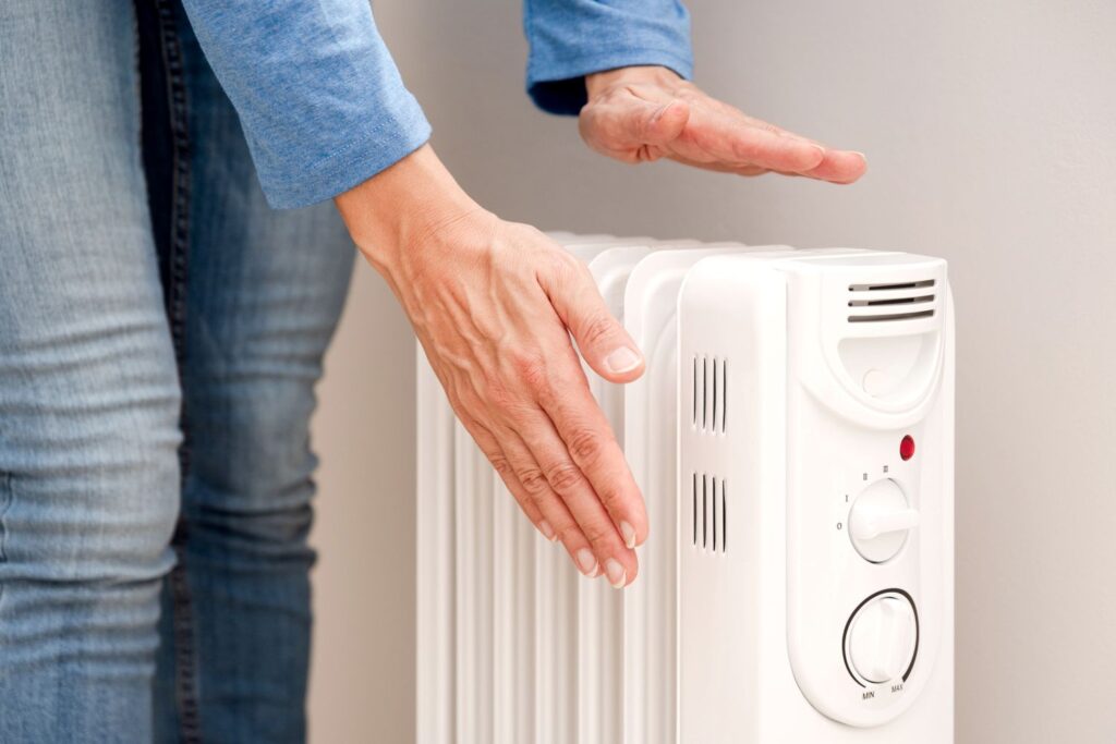 Person checking temperature of a white electric heater, emphasizing home heating efficiency and comfort.
