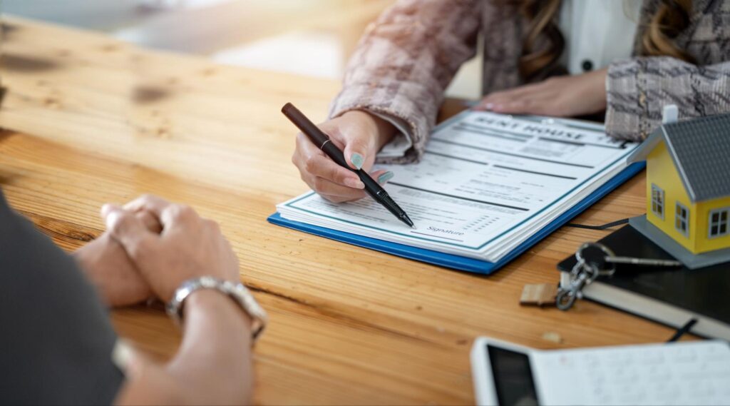 Person signing a document related to HVAC permits on a wooden table, with a small house model and keys nearby, illustrating the administrative process of furnace installation compliance.