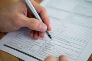 Person filling out a form with a pen, illustrating the process of completing HVAC service requests or permits related to heating installations.