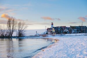 Snow-covered beach with calm water and a lighthouse in the background, reflecting seasonal beauty relevant to HVAC tips for winter homeowners.