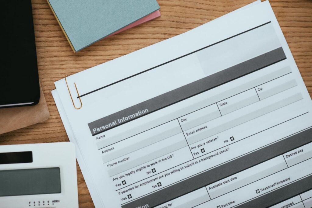 Personal information application form with fields for name, address, contact details, and employment eligibility, surrounded by stationery and a calculator, relevant to HVAC permit application processes in New Baltimore.