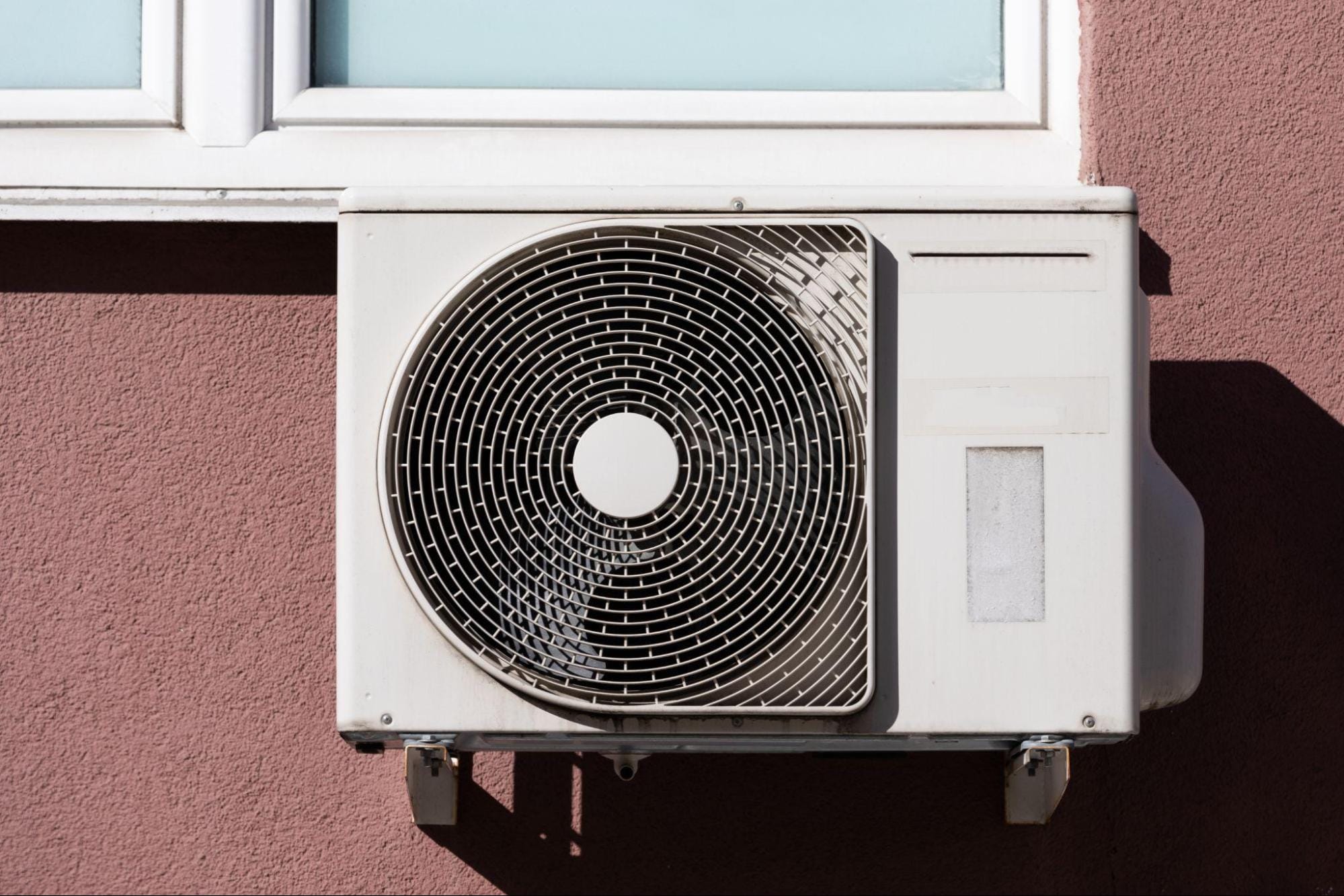 Outdoor air conditioner condenser installed beneath a window on a stucco home exterior