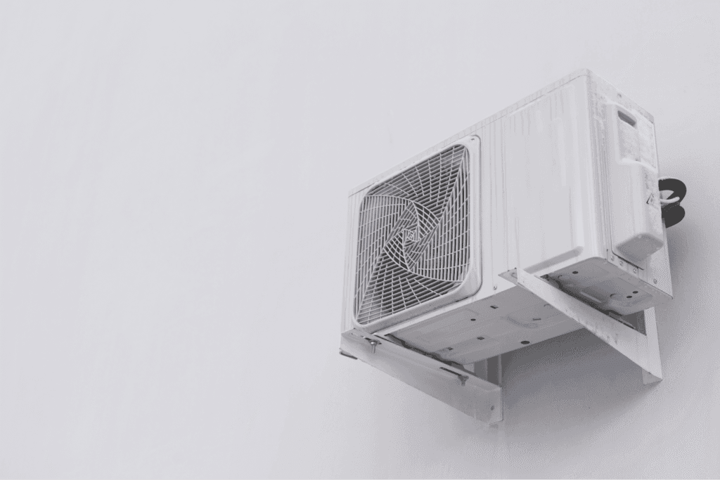 Outdoor AC condenser unit mounted on a wall bracket with clear space around it for proper airflow
