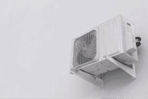 Outdoor AC condenser unit mounted on a wall bracket with clear space around it for proper airflow