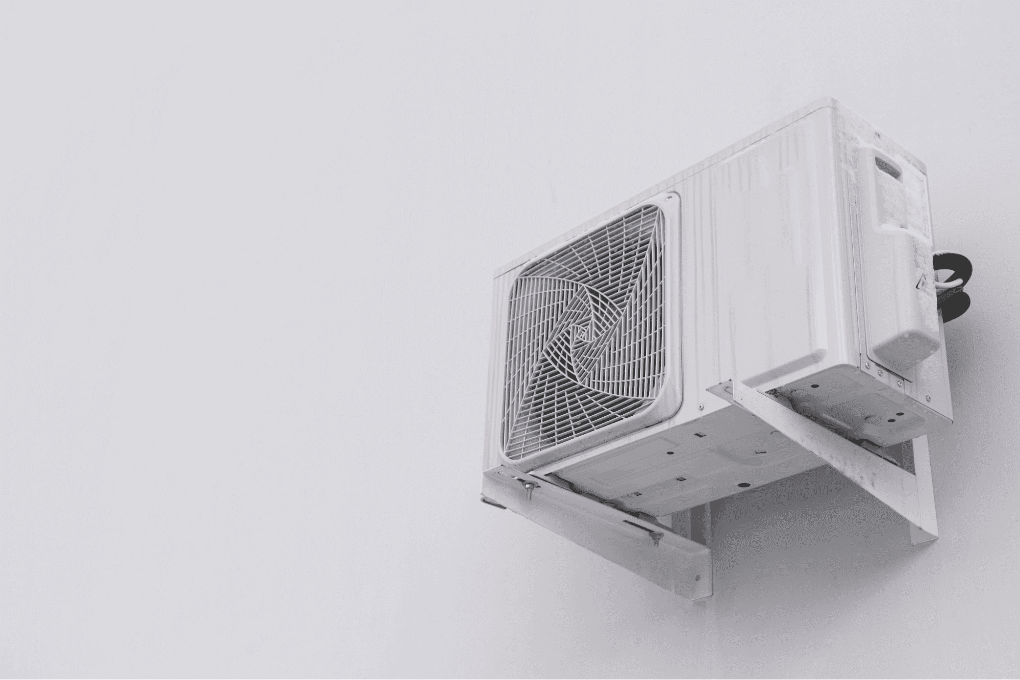 Outdoor AC condenser unit mounted on a wall bracket with clear space around it for proper airflow