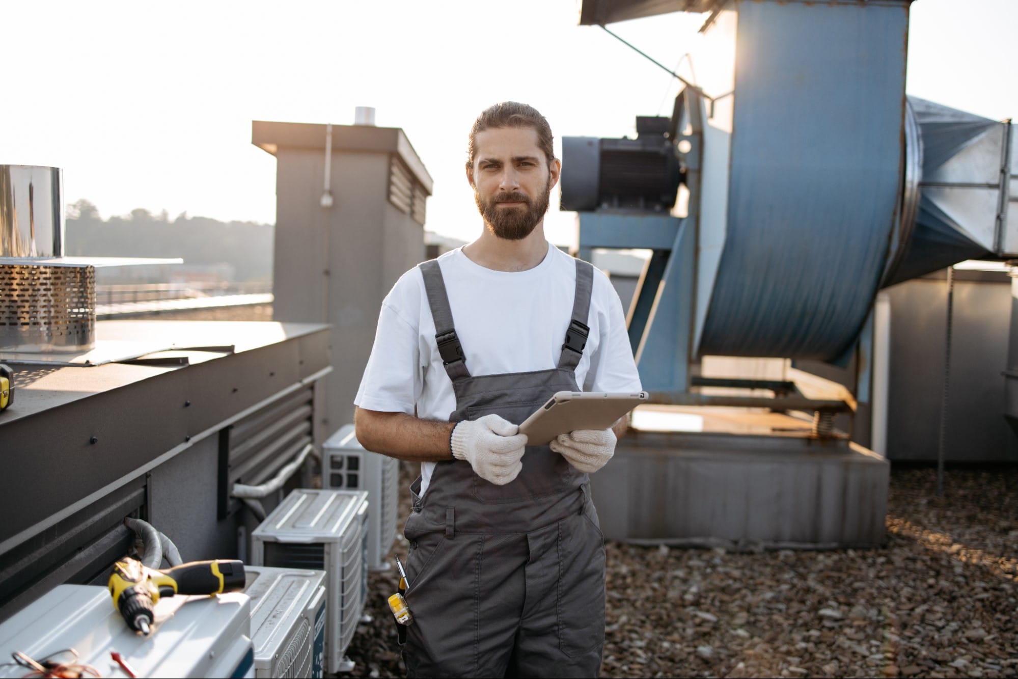 HVAC technician reviewing system inspection notes on a tablet near rooftop HVAC equipment in St. Clair County, MI