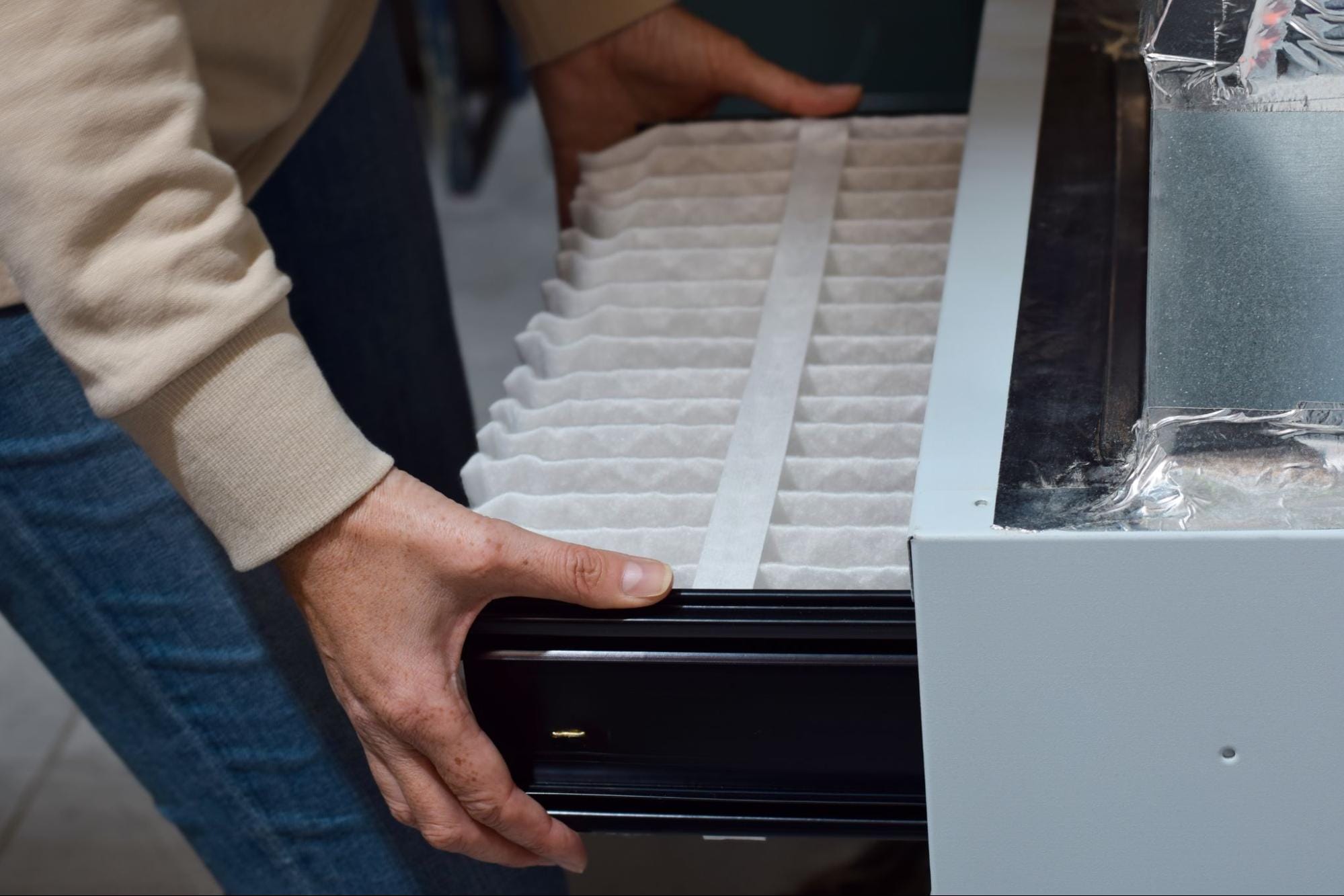 Technician sliding a new pleated air filter into a furnace filter slot