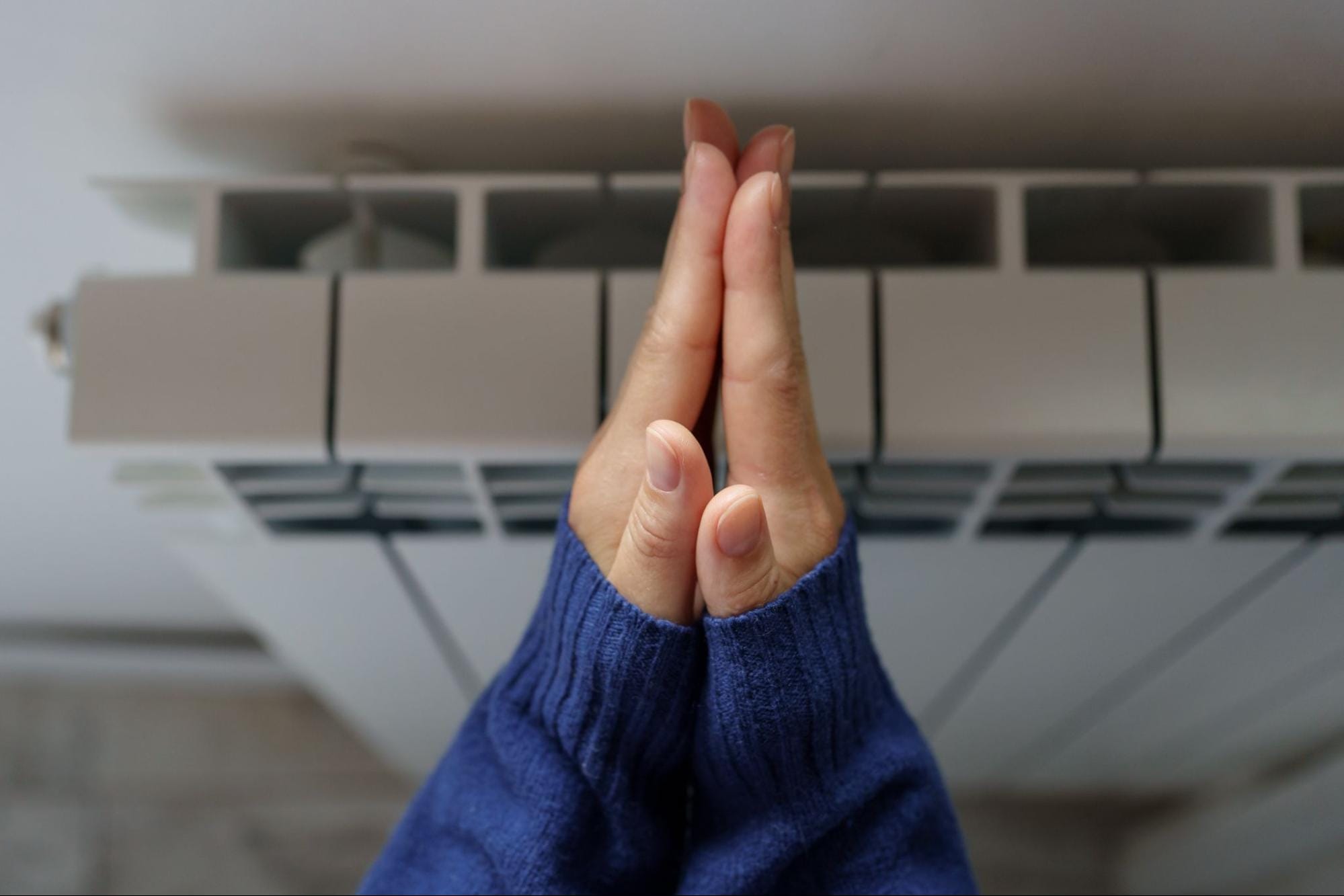 Hands warming near a wall-mounted home heating unit in Clay Township, MI