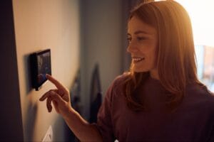Woman adjusting a smart thermostat touchscreen on the wall in Clay Township, MI