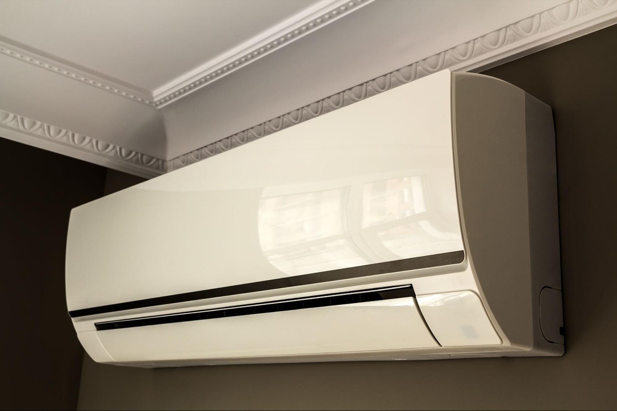 Wall-mounted white ductless mini split indoor unit installed near the ceiling beneath ornate crown molding, with a glossy front panel and horizontal air vent, professionally installed by S&P Heating in Clay Township, MI