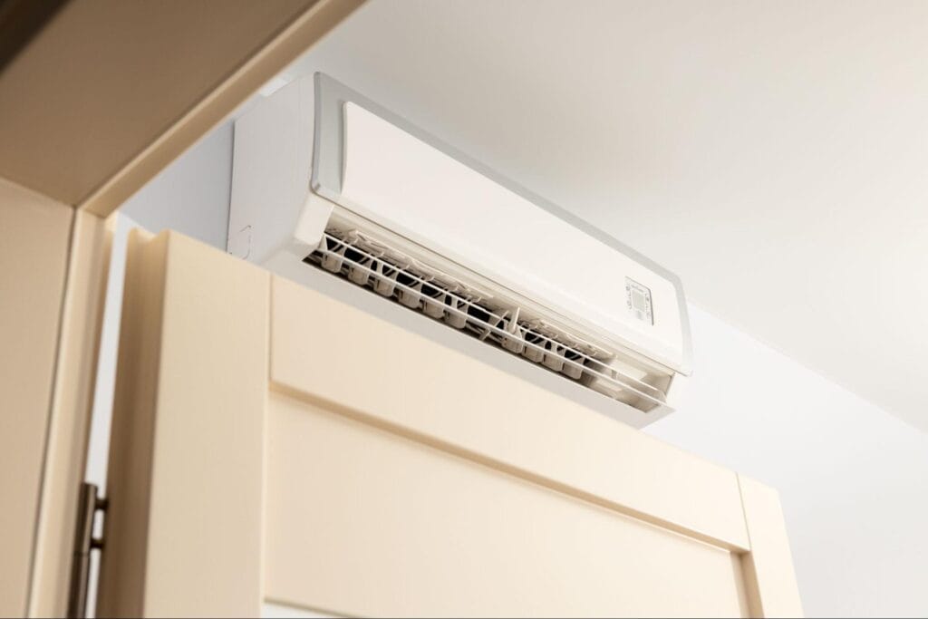 Close-up of a white ductless mini split indoor unit mounted high on a wall above a cream interior door, with the louvers open and the digital display panel visible, serviced by S&P Heating in Clay Township, MI